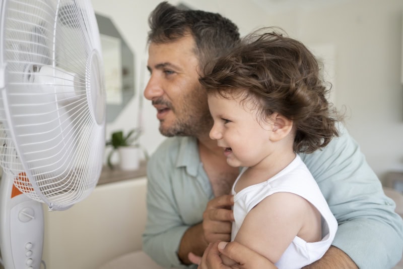 Common AC Problems and Solutions. Father child is front of electric fan on hot summer day.