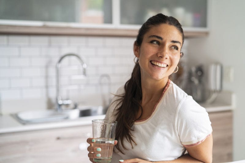 Water Softener. Woman smiling holding a glass of water in her kitchen.